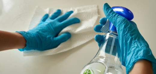 A person wearing latex gloves uses spray and a paper towel to clean a white surface