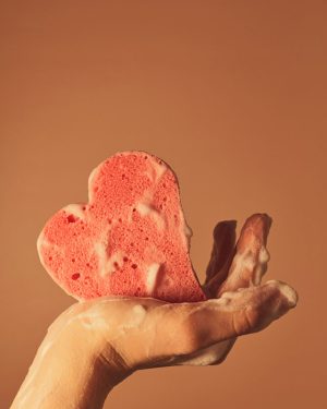 Soapy hand holding a heart-shaped sponge